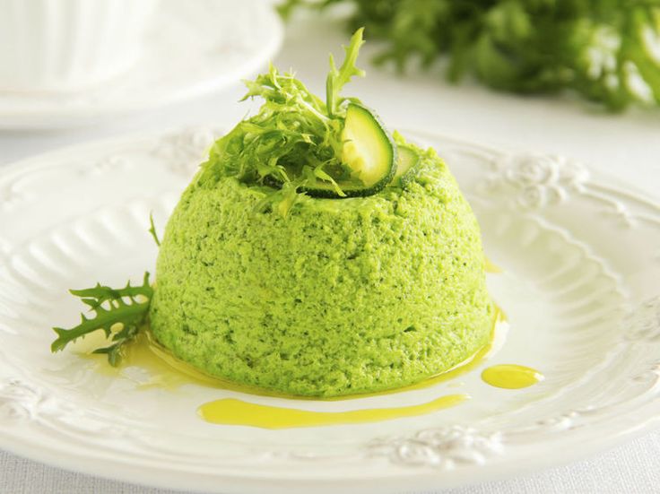 A dome-shaped green pea mousse garnished with herbs and olive oil.