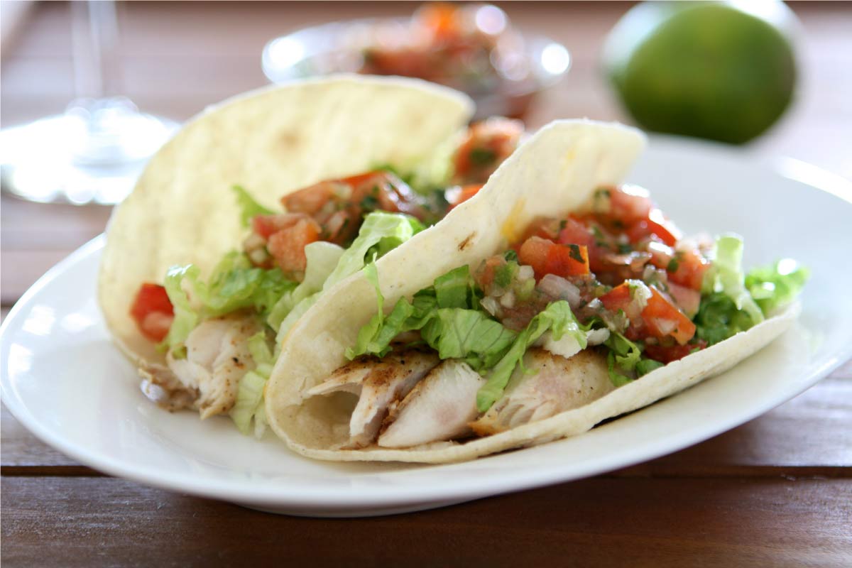 Two chicken tacos topped with salsa and avocado on a plate.