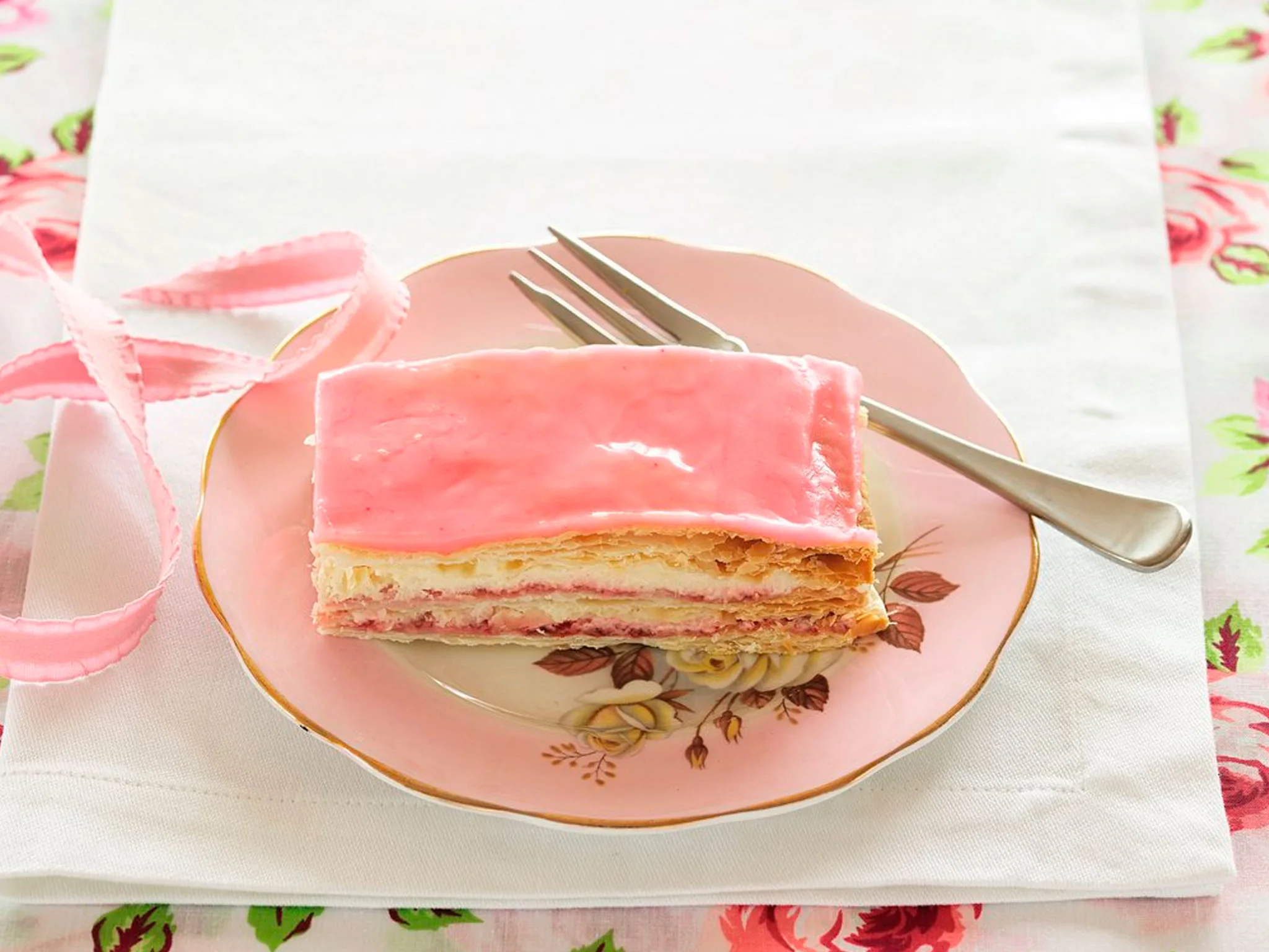 A slice of layered pink frosted cake on a pink plate.