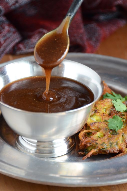Rich brown gravy being poured into a silver bowl with fried food on the side.