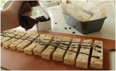 Rows of dessert bars drizzled with chocolate on a wooden surface.