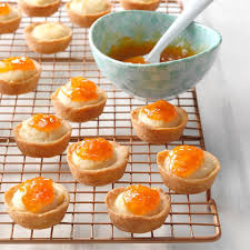 Mini tartlets topped with orange marmalade on a cooling rack.