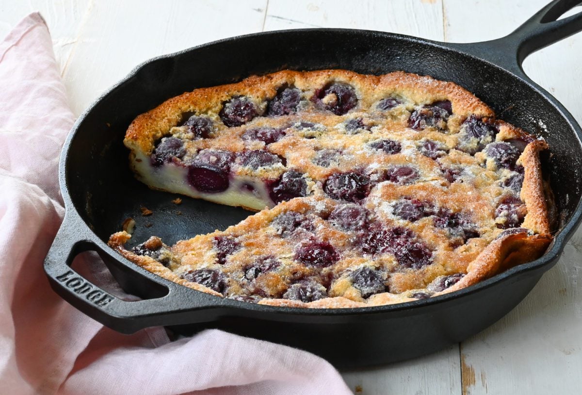 Cherry clafoutis baked in a cast iron skillet with a slice removed.