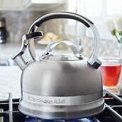 Stainless steel kettle on a stove with a red cup in the background.