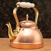 A vintage copper kettle with a white handle on a wooden surface.