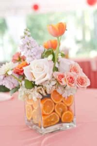 A vibrant floral arrangement with orange slices in a glass vase.