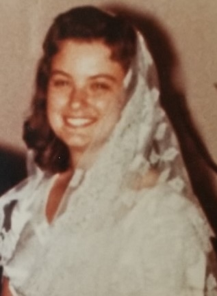 A smiling woman wearing a white veil, possibly a bride.