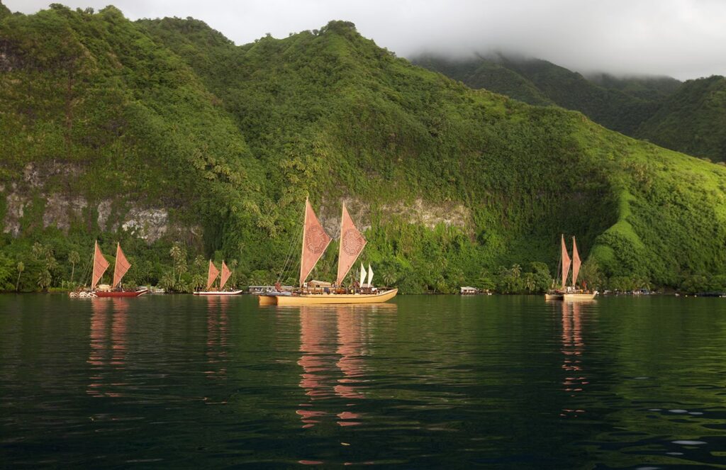 Traditional sailboats on calm water near lush green mountains.