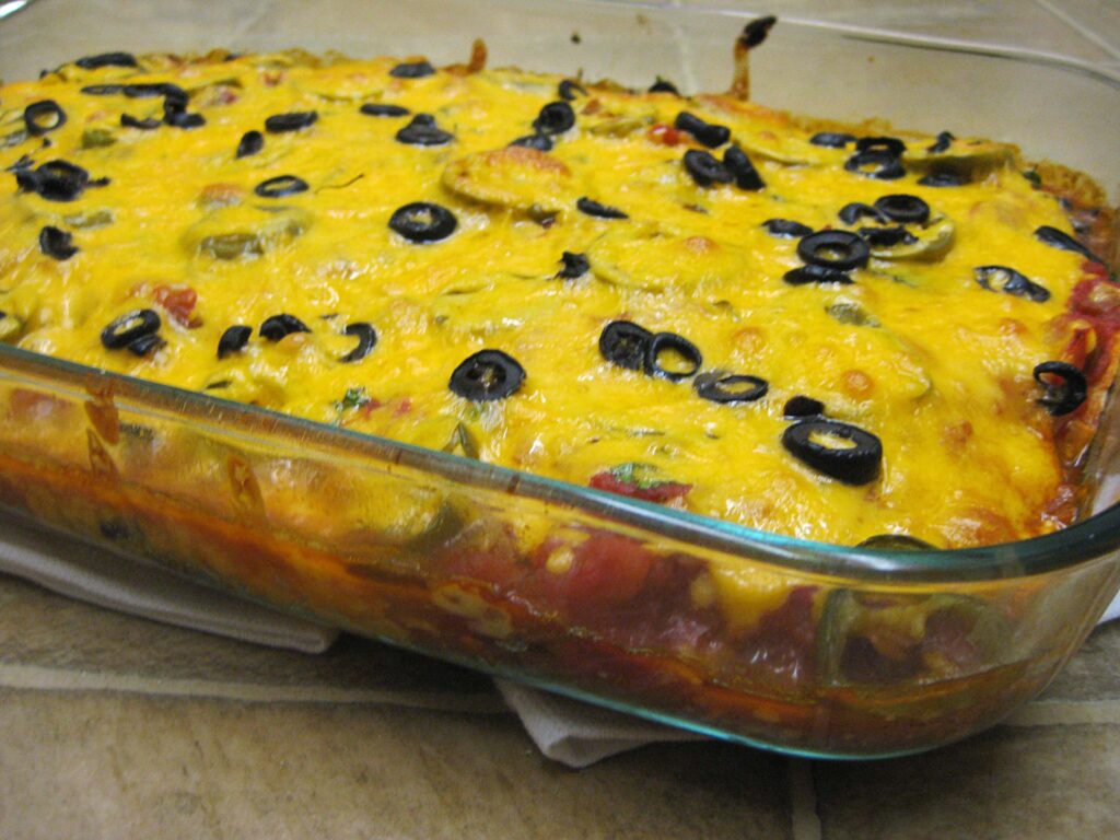 A cheesy baked casserole topped with black olives in a glass dish.