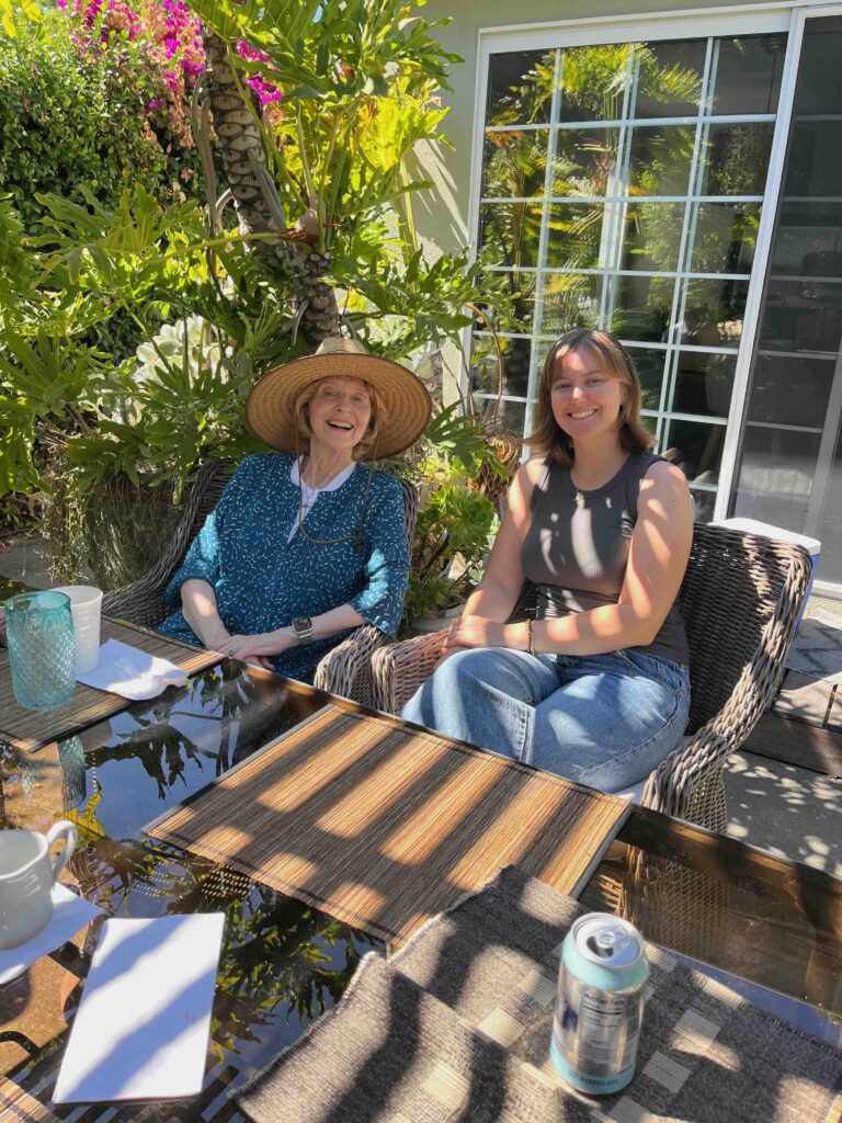 Two women sitting outdoors, enjoying a sunny day with plants around.